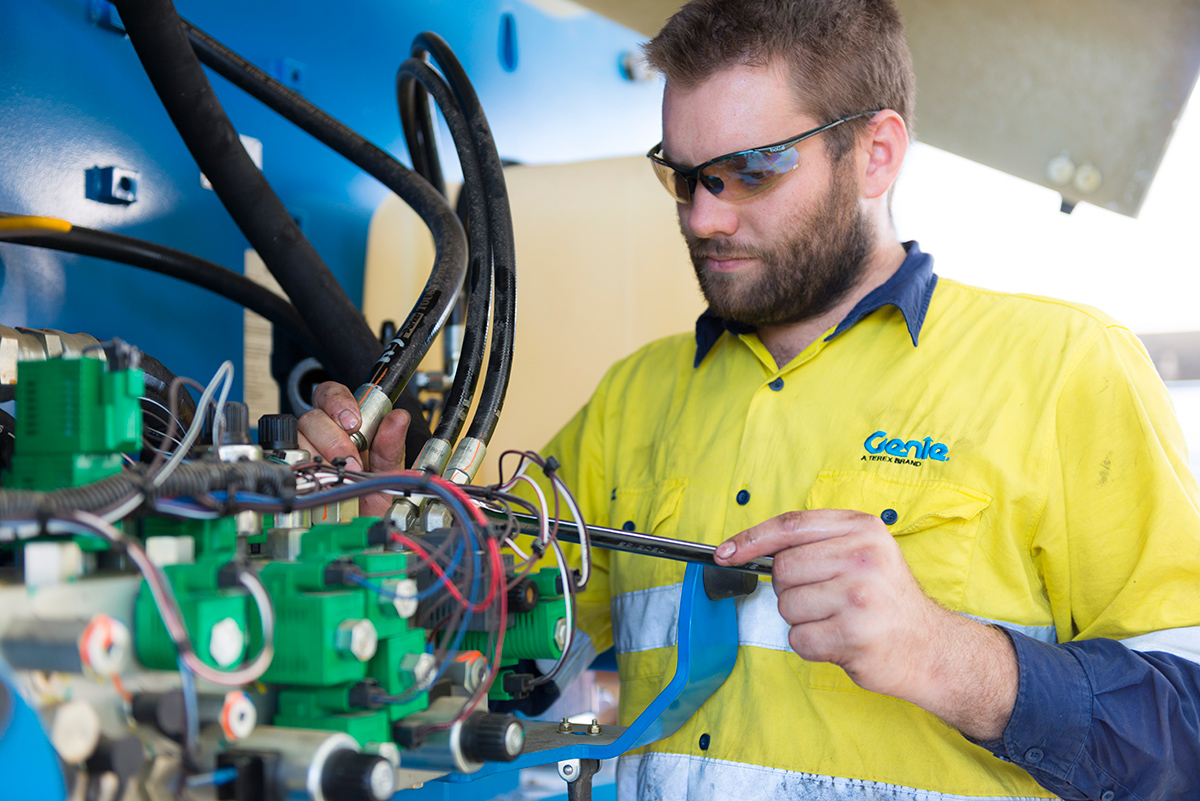 Genie service technician inspecting hydraulic hoses during scheduled maintenance